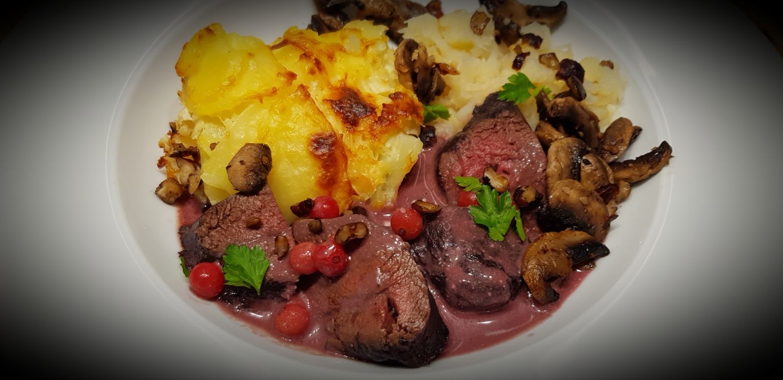 Rôti de chevreuil servi avec sauce grand veneur, gratin doré, champignons poêlés et airelles.